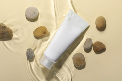 Photo of Tube of face cleansing product and stones in water against beige background, flat lay