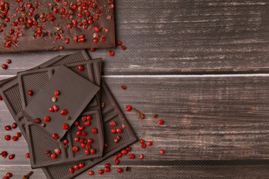 Delicious chocolate and red peppercorns on wooden table, flat lay. Space for text