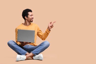 Photo of Happy man with laptop pointing at something on beige background. Space for text