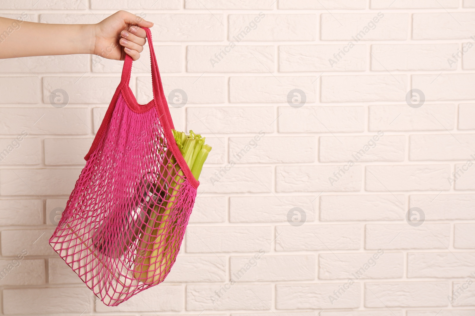 Photo of Woman holding net bag with different items against brick wall, closeup and space for text. Conscious consumption