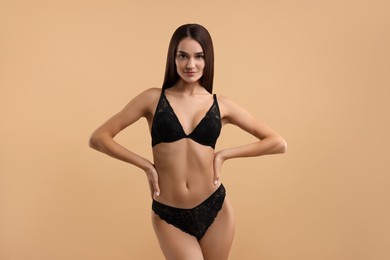 Photo of Young woman in elegant black underwear on beige background