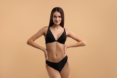 Young woman in elegant black underwear on beige background