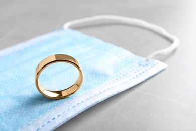 Photo of Protective mask and wedding ring on grey table, closeup. Divorce during coronavirus quarantine