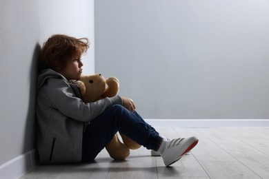 Photo of Child abuse. Upset boy with toy sitting on floor near grey wall, space for text