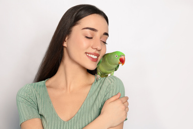 Photo of Young woman with Alexandrine parakeet on light background. Cute pet