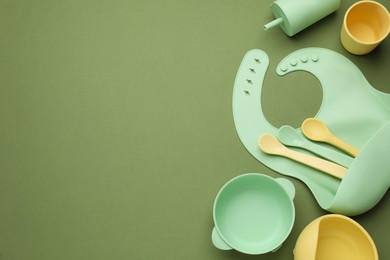 Flat lay composition with baby feeding accessories and bib on green background, space for text