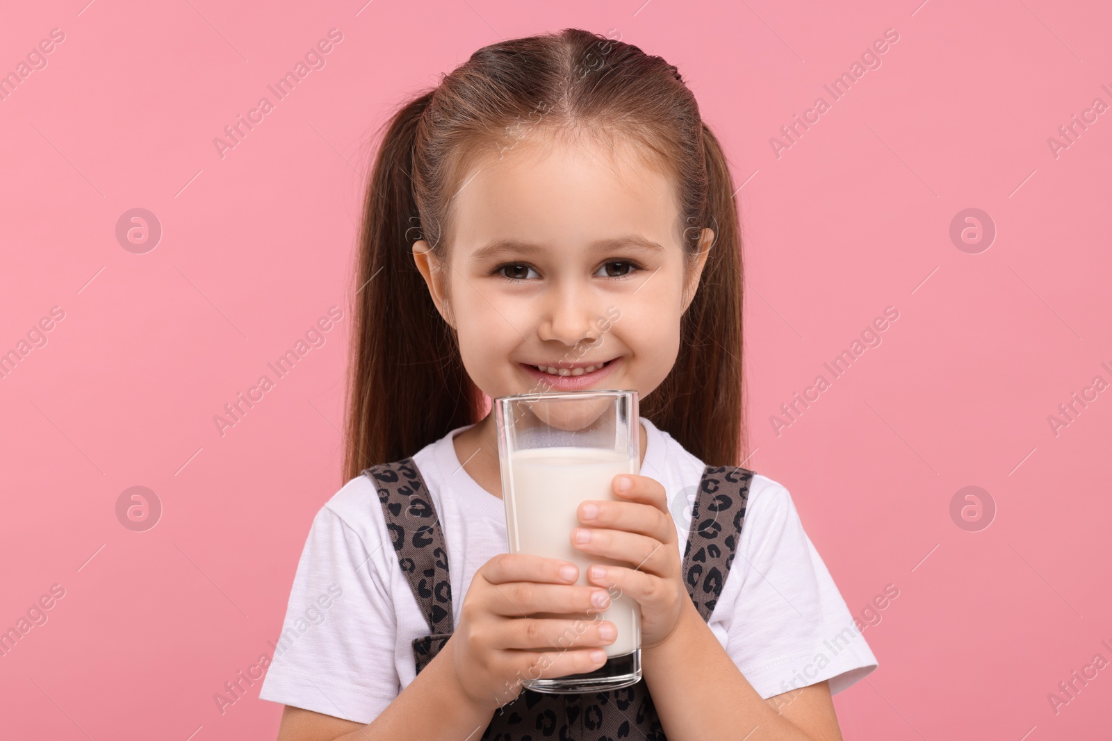 Photo of Cute girl with glass of fresh milk on pink background