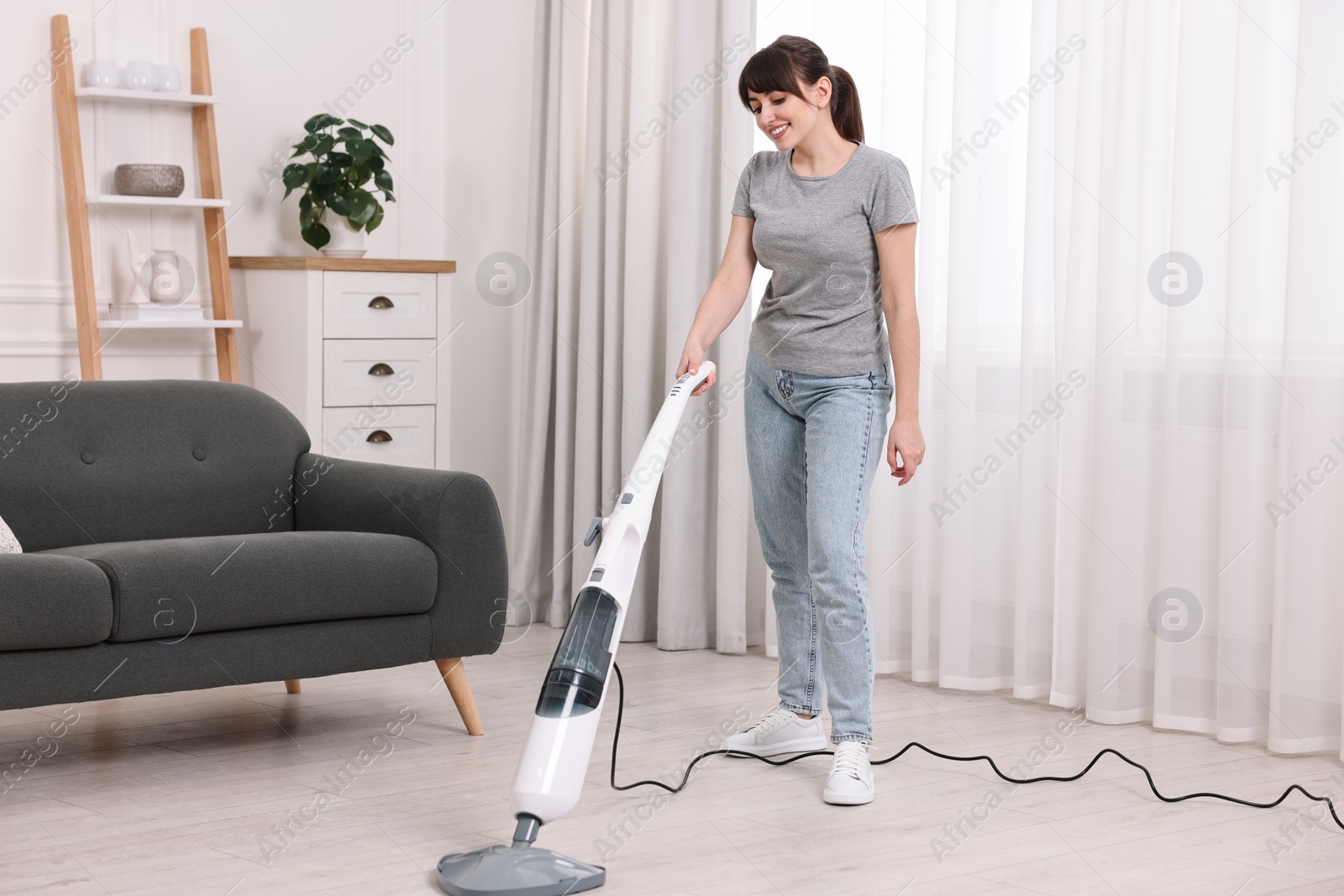 Photo of Happy young housewife cleaning floor with steam mop at home