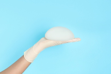 Photo of Doctor holding silicone implant for breast augmentation on color background, space for text. Cosmetic surgery