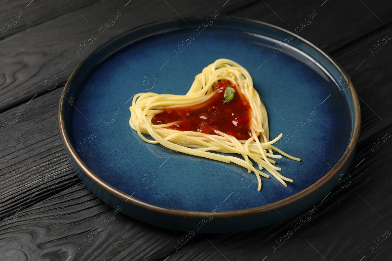 Photo of Heart made with spaghetti and sauce on black wooden table