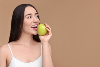 Beautiful young woman with apple on beige background. Space for text