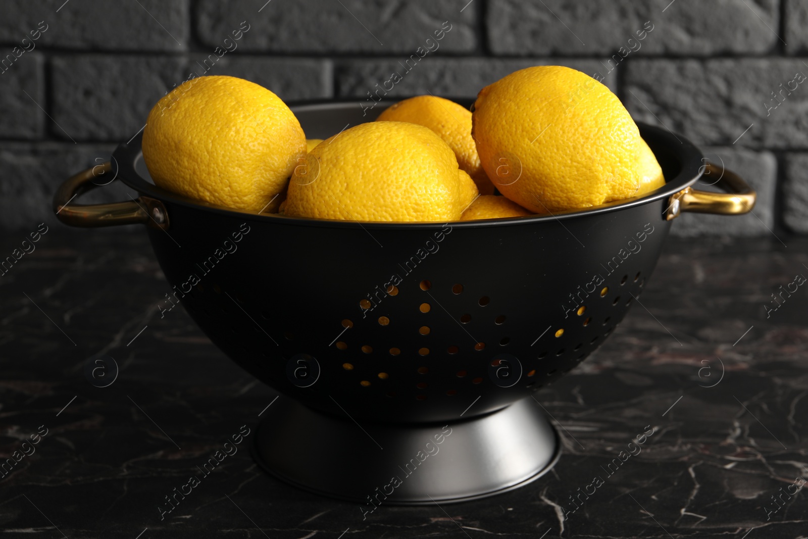 Photo of One colander with fresh lemons on black marble table, closeup