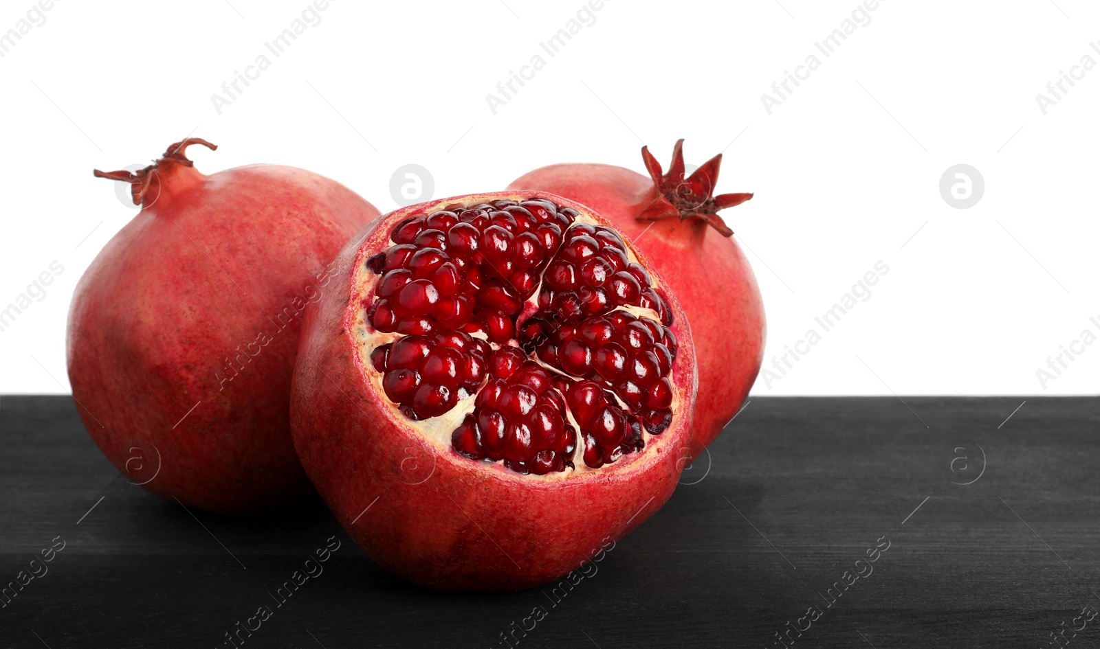 Photo of Fresh pomegranates on black wooden table against white background, space for text