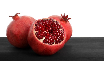 Fresh pomegranates on black wooden table against white background, space for text