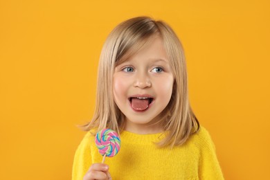 Portrait of cute little girl with lollipop on orange background