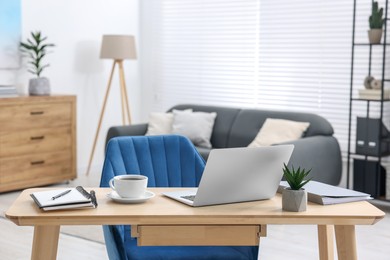 Photo of Home workspace. Laptop, cup of coffee and stationery on wooden desk indoors