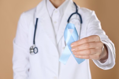 Photo of International Psoriasis Day. Doctor with light blue ribbon as symbol of support on beige background, closeup
