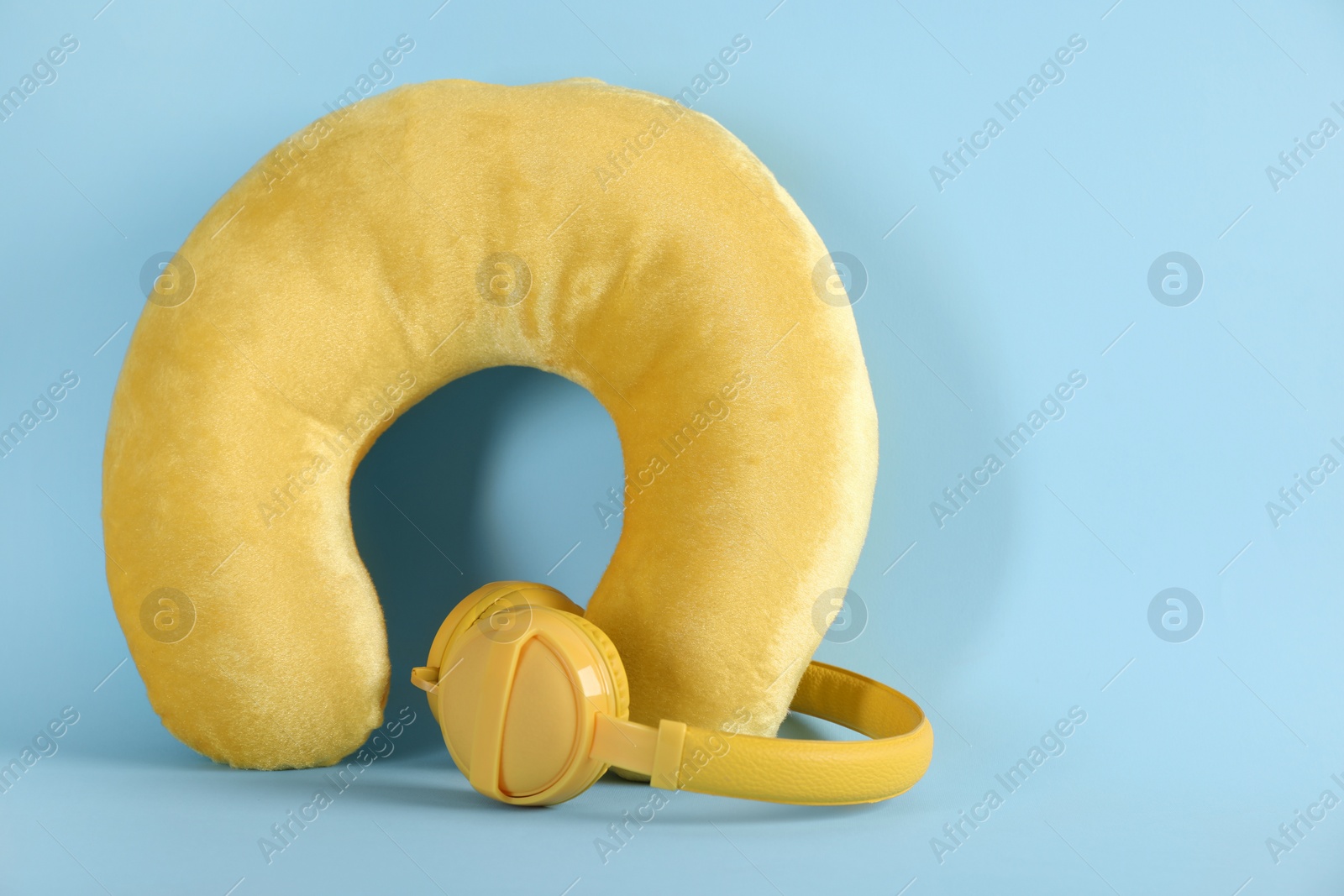 Photo of Yellow travel pillow and headphones on light blue background, space for text