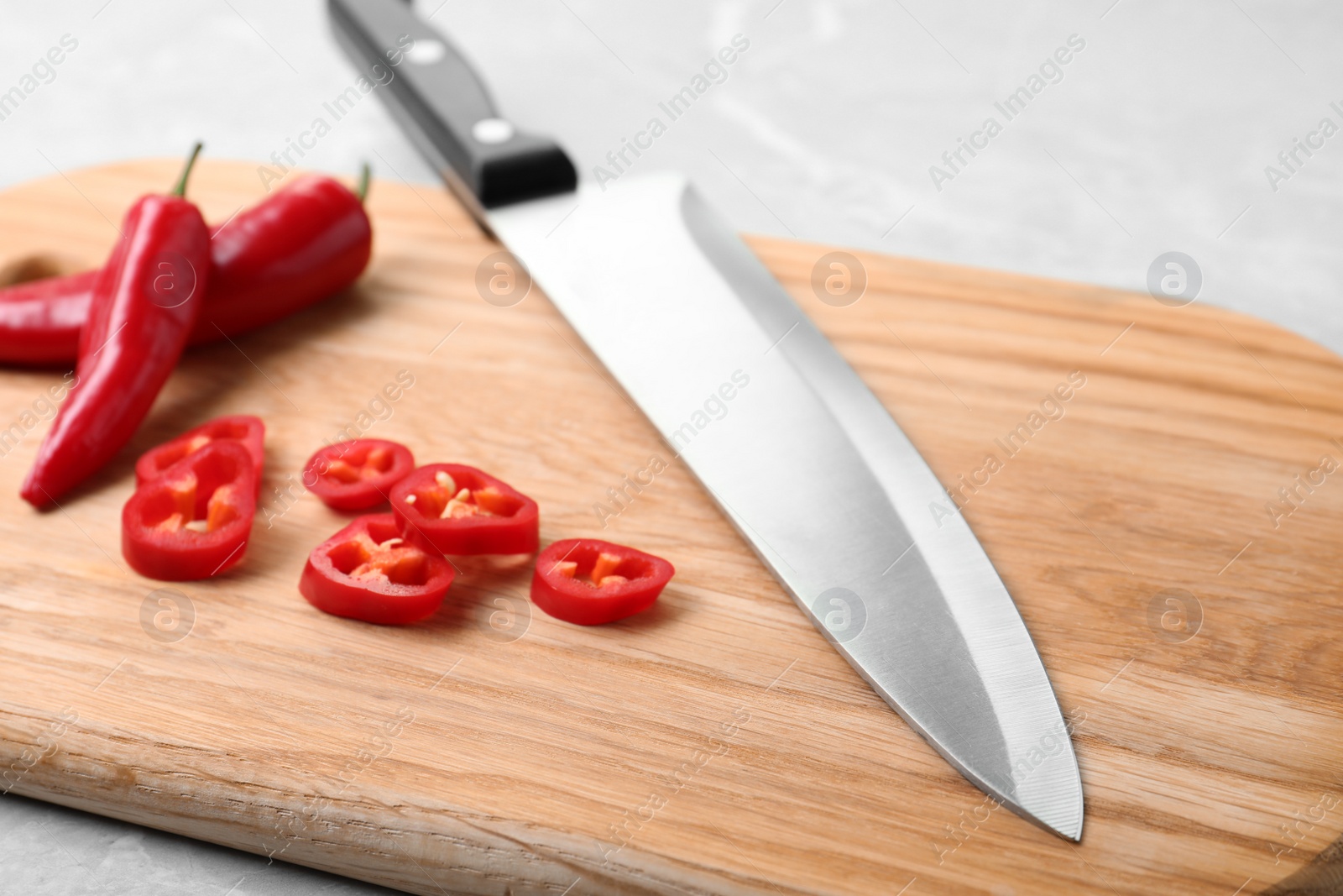 Photo of Wooden board with sharp knife and cut chili peppers on table, closeup