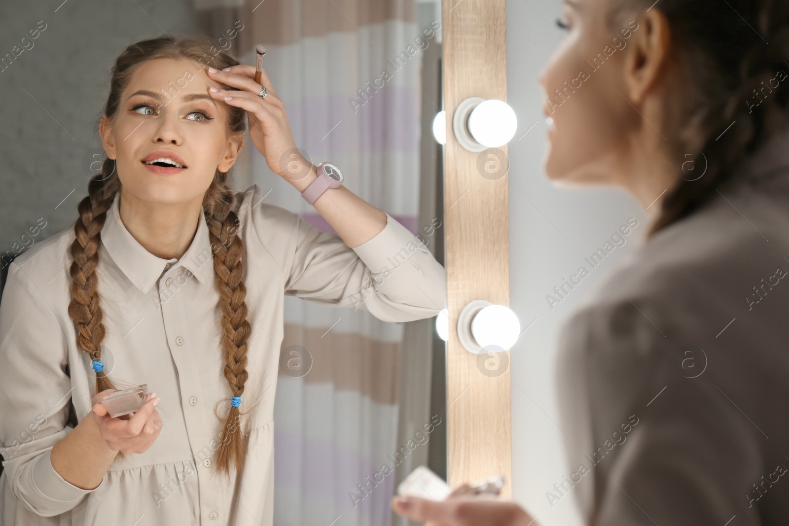 Photo of Portrait of beautiful woman applying makeup near mirror indoors