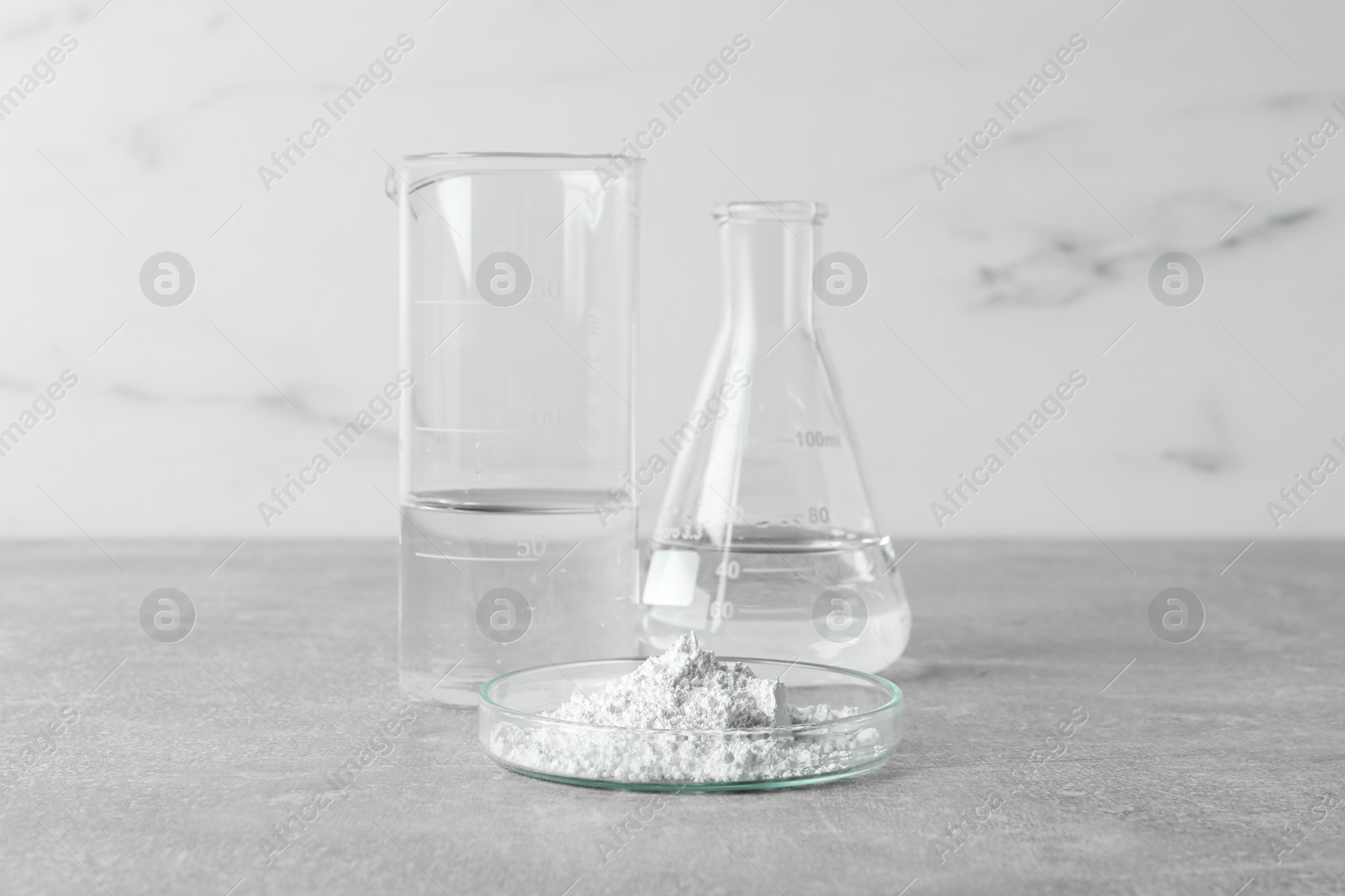 Photo of Petri dish with calcium carbonate powder and laboratory glassware on light grey table