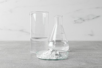 Photo of Petri dish with calcium carbonate powder and laboratory glassware on light grey table