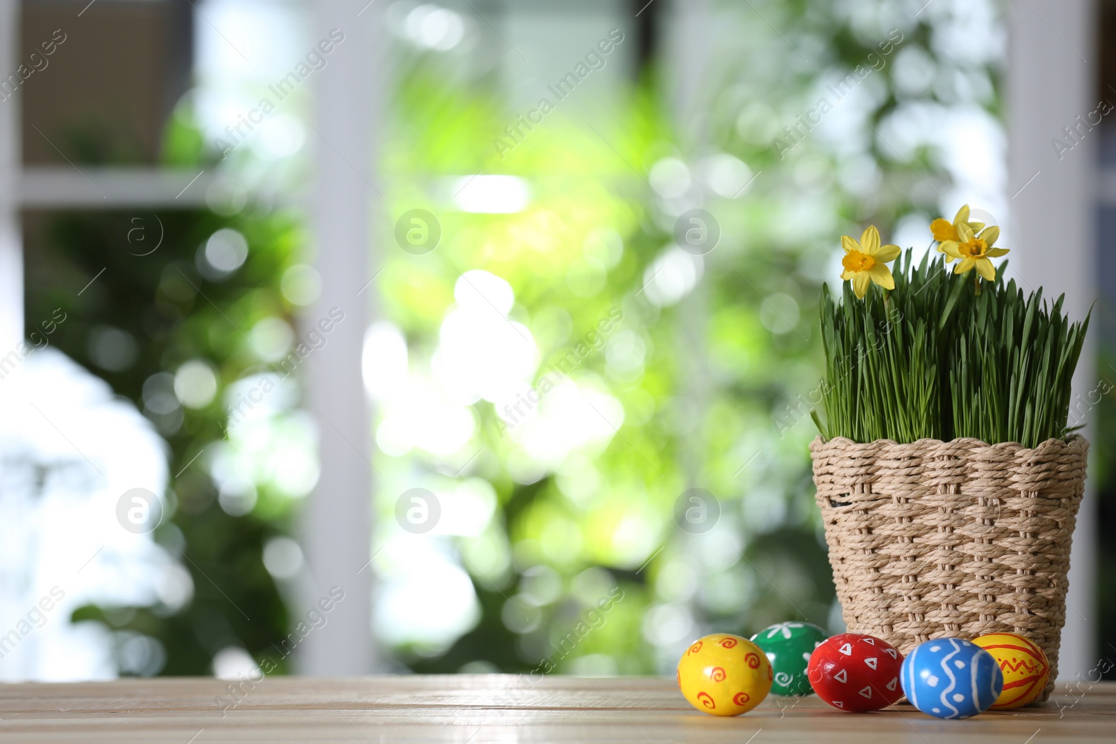 Photo of Colorful Easter eggs and flowers on wooden table against blurred green background. Space for text