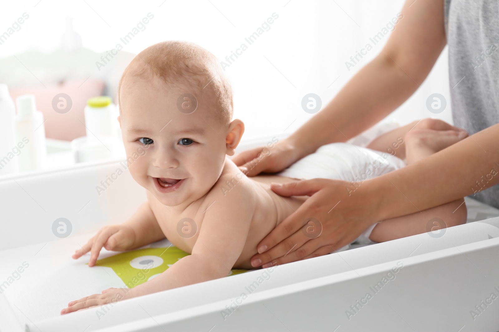 Photo of Young woman massaging cute baby on changing table