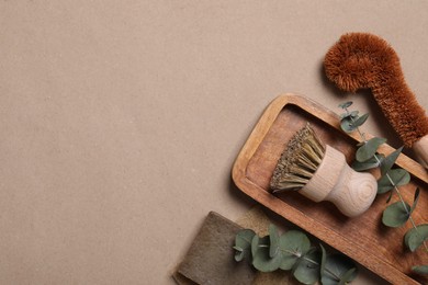 Cleaning brushes, soap bar, sponge and eucalyptus leaves on pale brown background, top view. Space for text