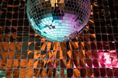 Photo of Shiny disco ball against foil party curtain under turquoise and orange light. Space for text