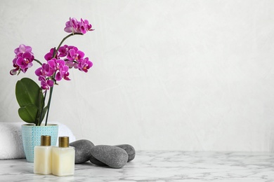 Photo of Spa accessories and blooming orchid on marble table against light background, space for text