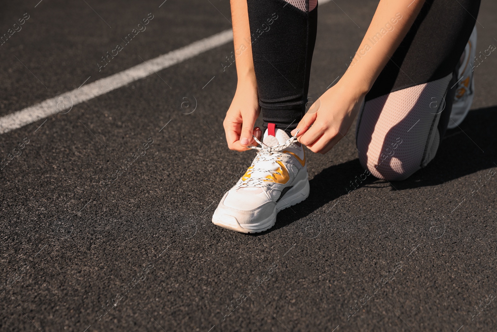 Photo of Young woman tying shoelaces at stadium on sunny day