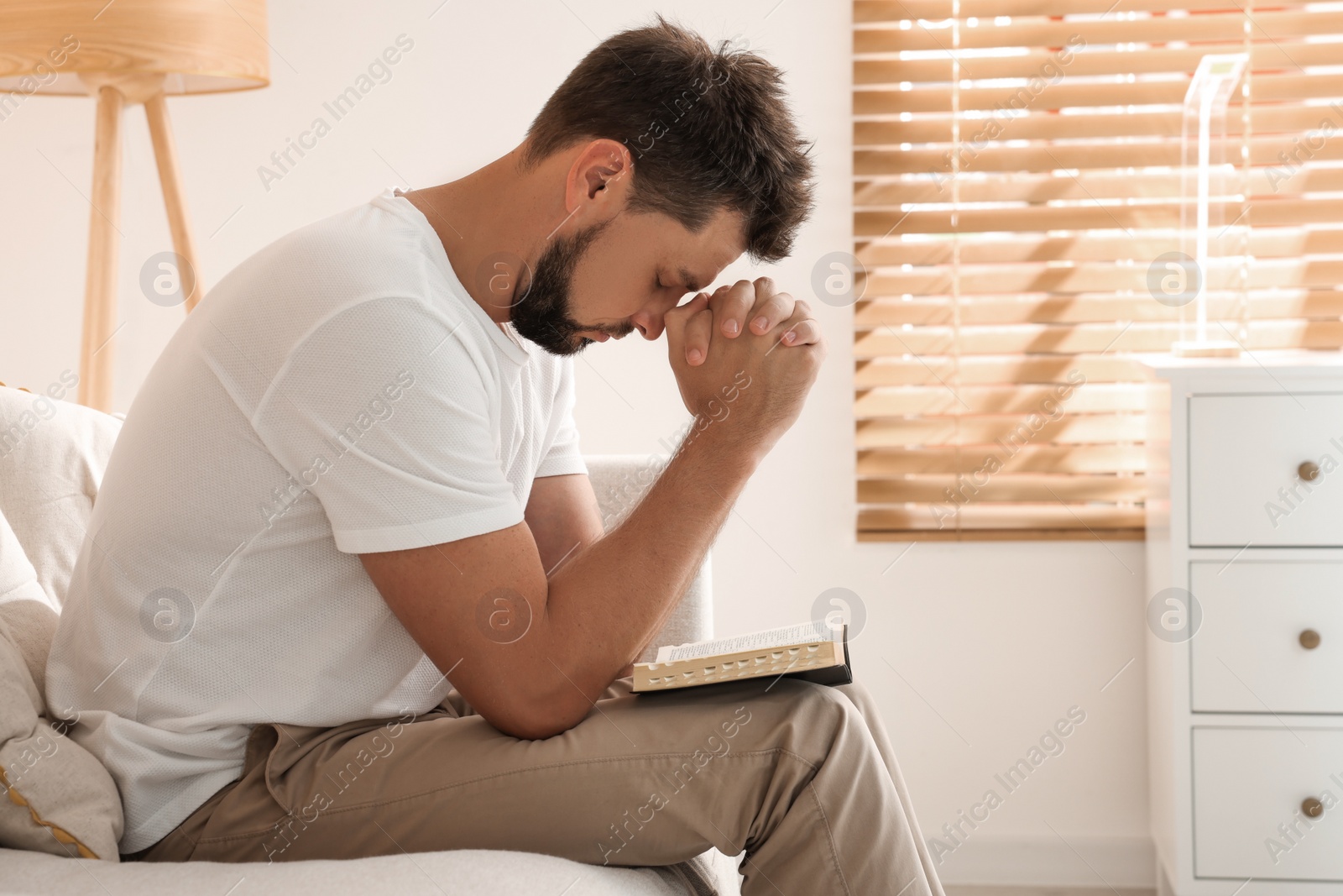 Photo of Religious man with Bible praying indoors. Space for text