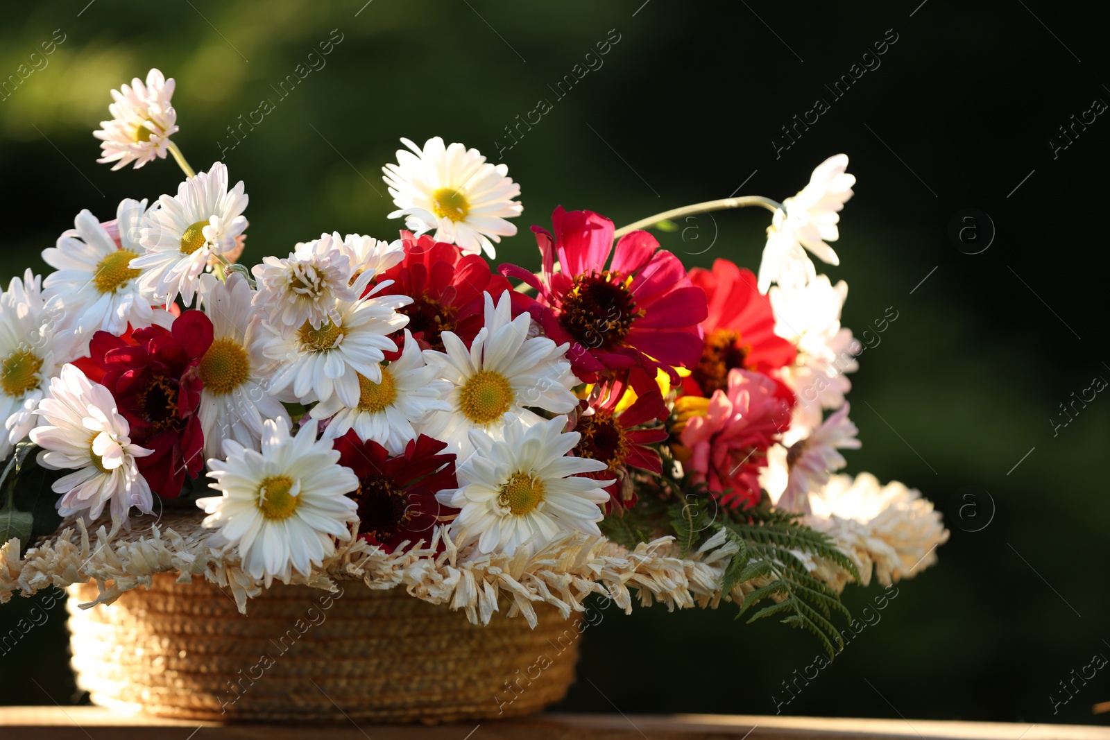 Photo of Beautiful wild flowers in wicker basket on wooden table against blurred background