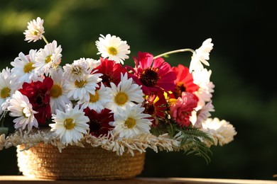 Beautiful wild flowers in wicker basket on wooden table against blurred background