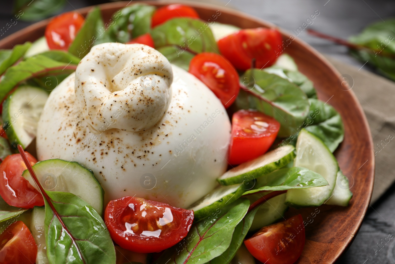 Photo of Delicious burrata salad with tomatoes and cucumbers on plate, closeup