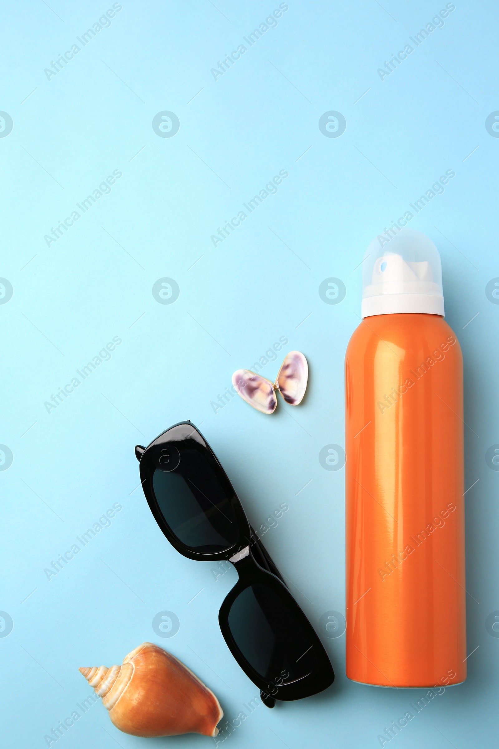 Photo of Bottle of sunscreen, sunglasses and seashells on light blue background, flat lay. Space for text