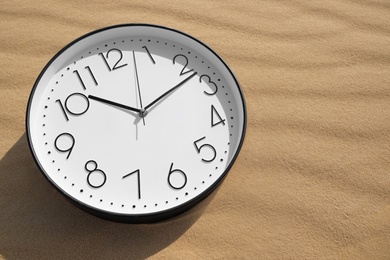 Stylish clock on sand in desert, above view