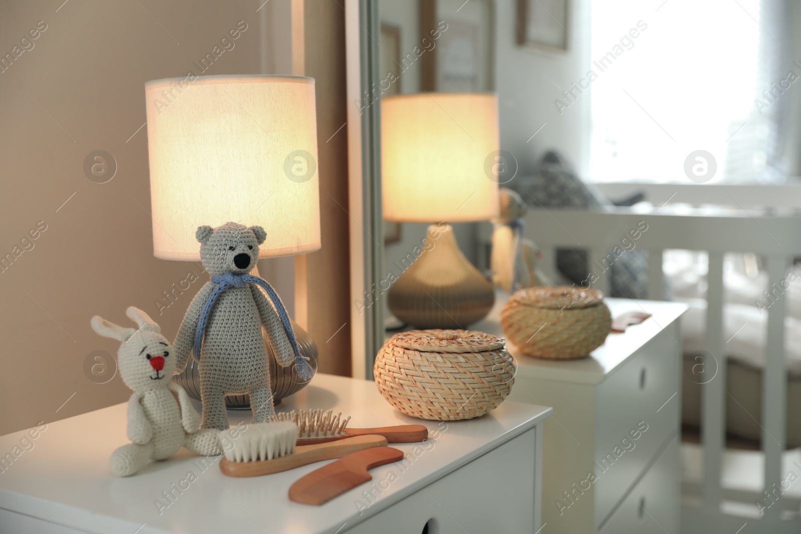 Photo of Toys, lamp and hair brushes on chest of drawers near mirror indoors. Interior elements