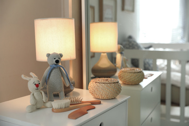 Toys, lamp and hair brushes on chest of drawers near mirror indoors. Interior elements