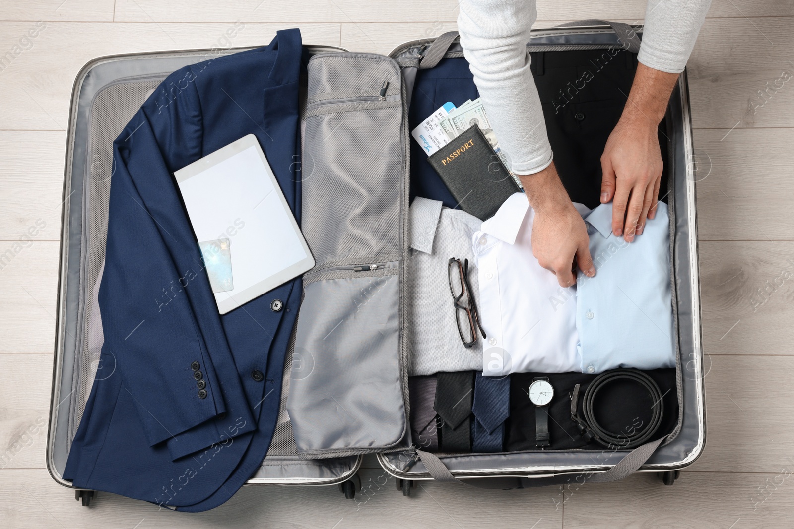 Photo of Man packing suitcase for business trip on wooden floor, top view