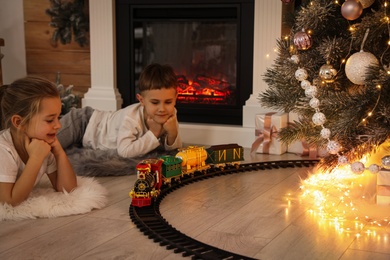 Photo of Children playing with colorful train toy in room decorated for Christmas