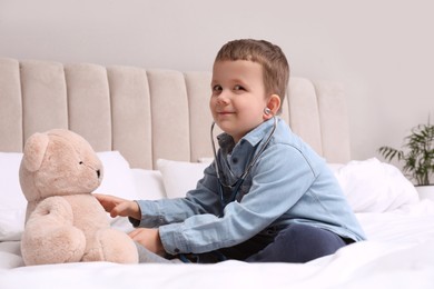 Photo of Cute little boy playing with stethoscope and toy bear in bedroom. Future pediatrician