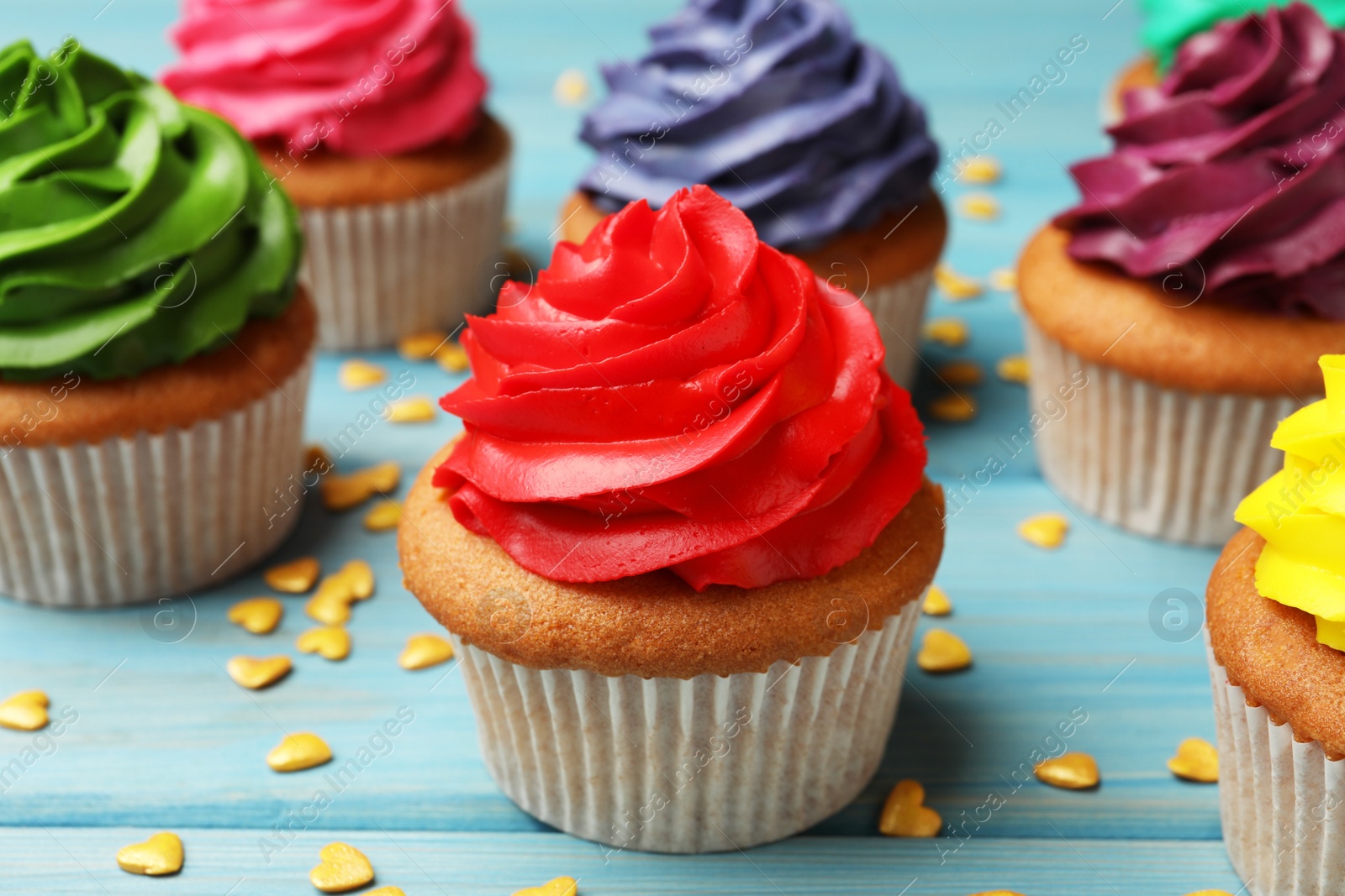 Photo of Delicious colorful cupcakes and heart shaped sprinkles on light blue wooden table, closeup