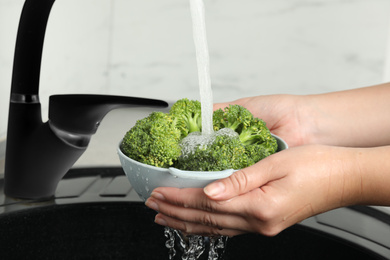 Photo of Woman washing fresh green broccoli in kitchen sink, closeup