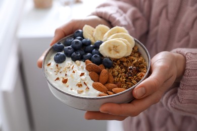 Woman holding bowl of tasty granola indoors, closeup