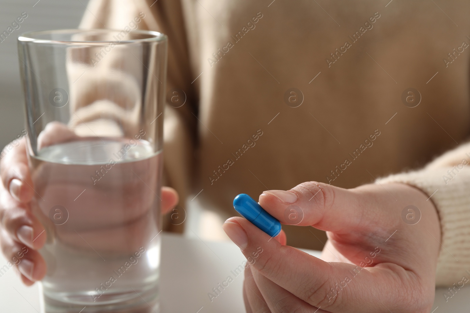 Photo of Woman with glass of water and pill at white table, closeup