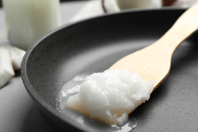 Photo of Frying pan with coconut oil and wooden spatula on grey table, closeup. Healthy cooking