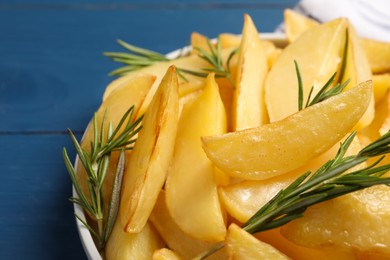 Photo of Plate with tasty baked potato wedges and rosemary on blue table, closeup
