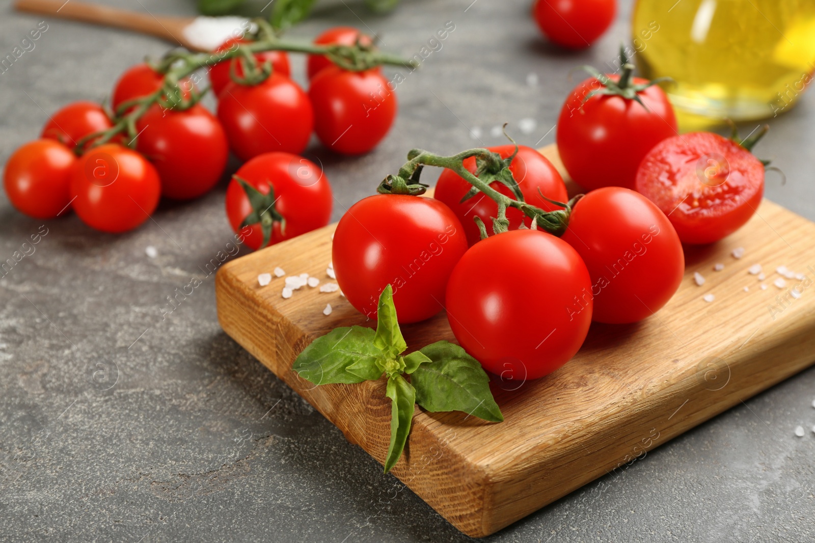 Photo of Fresh ripe cherry tomatoes, salt and basil on grey table